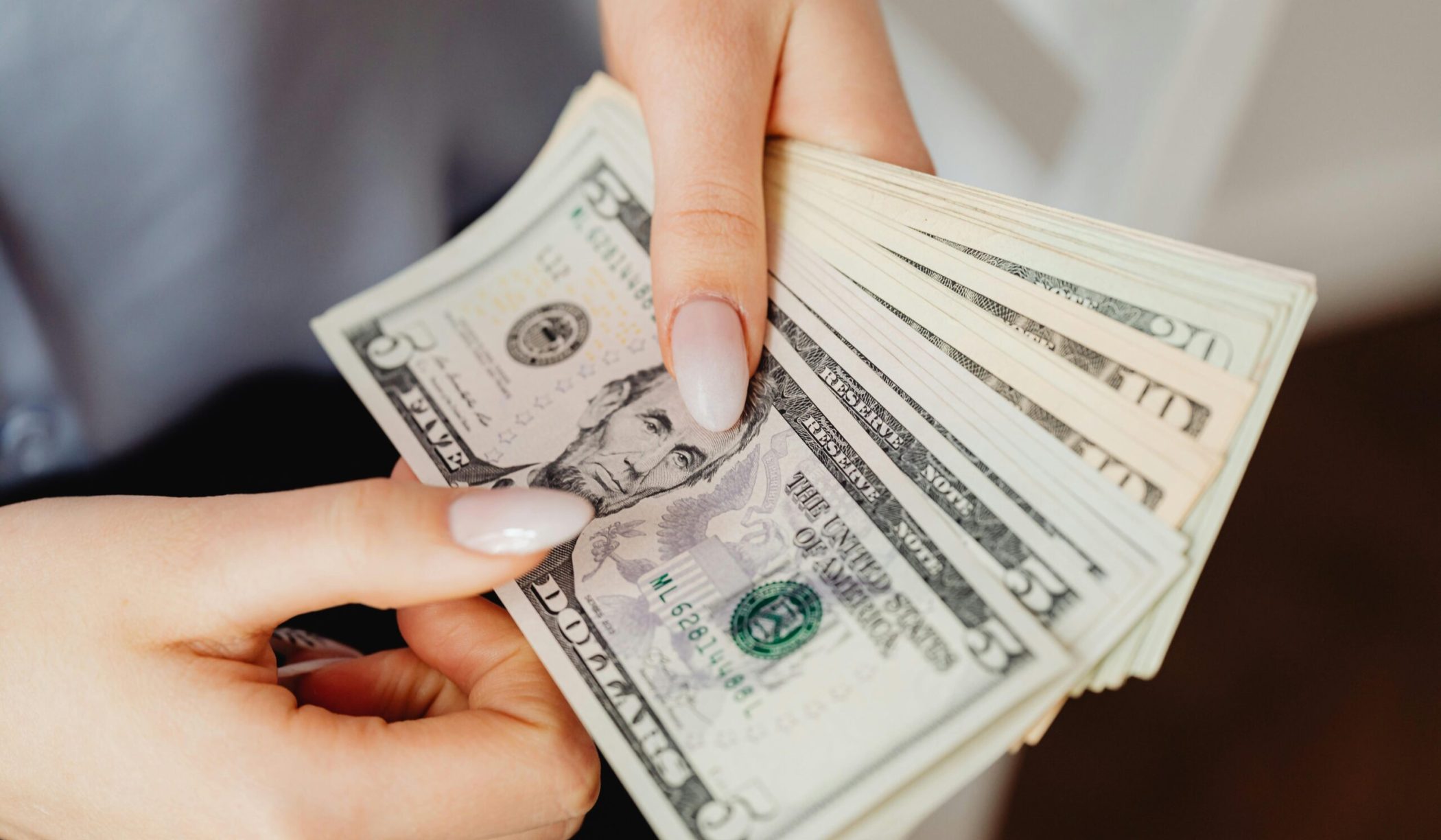 Hands count US dollar bills, showcasing finance and cash handling concepts.